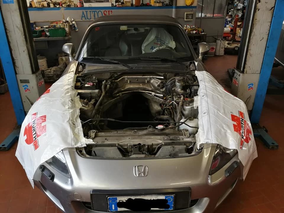 Vettura con il vano motore aperto e protezioni sulla carrozzeria durante la riparazione
